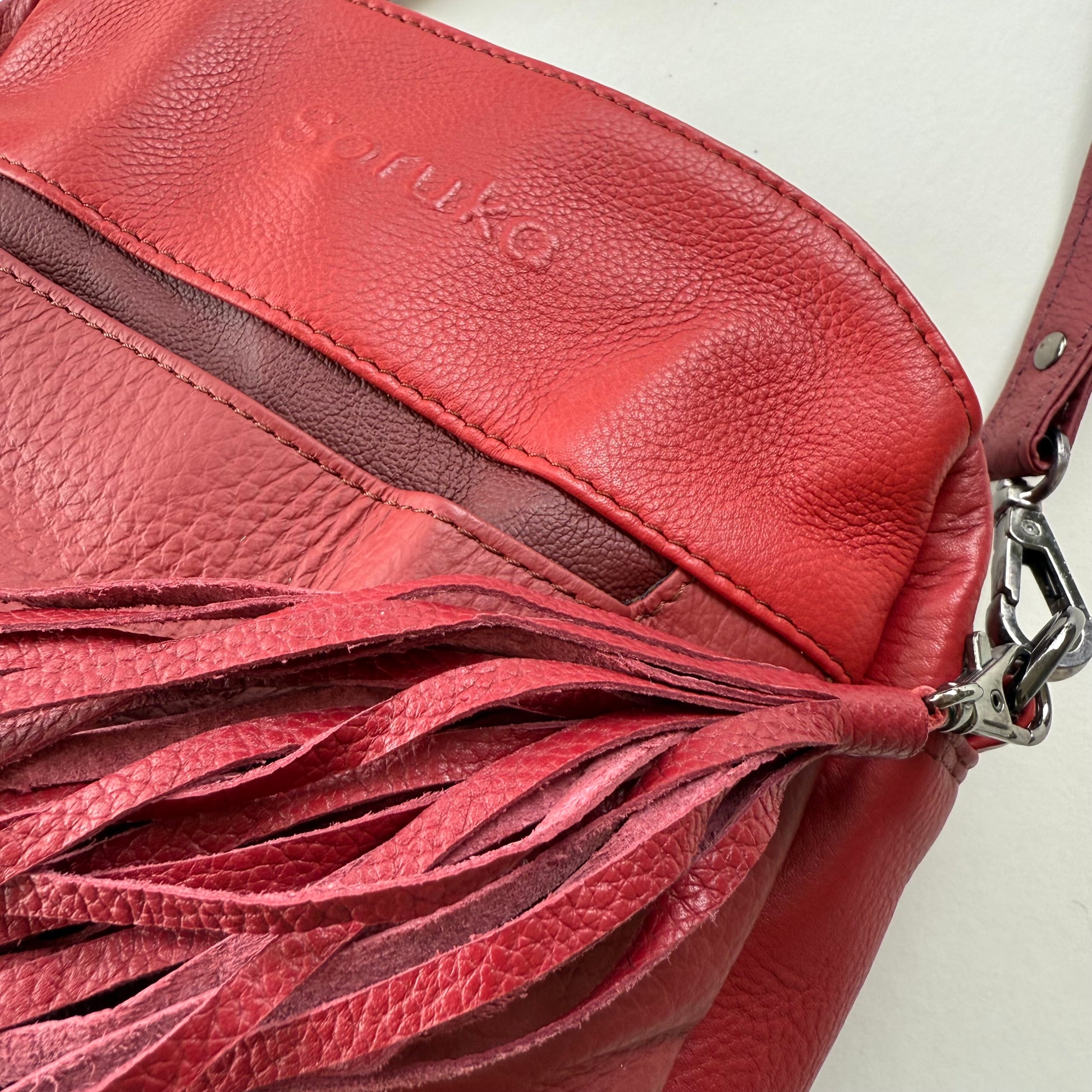 Red leather handbag with tassel detail on a white background