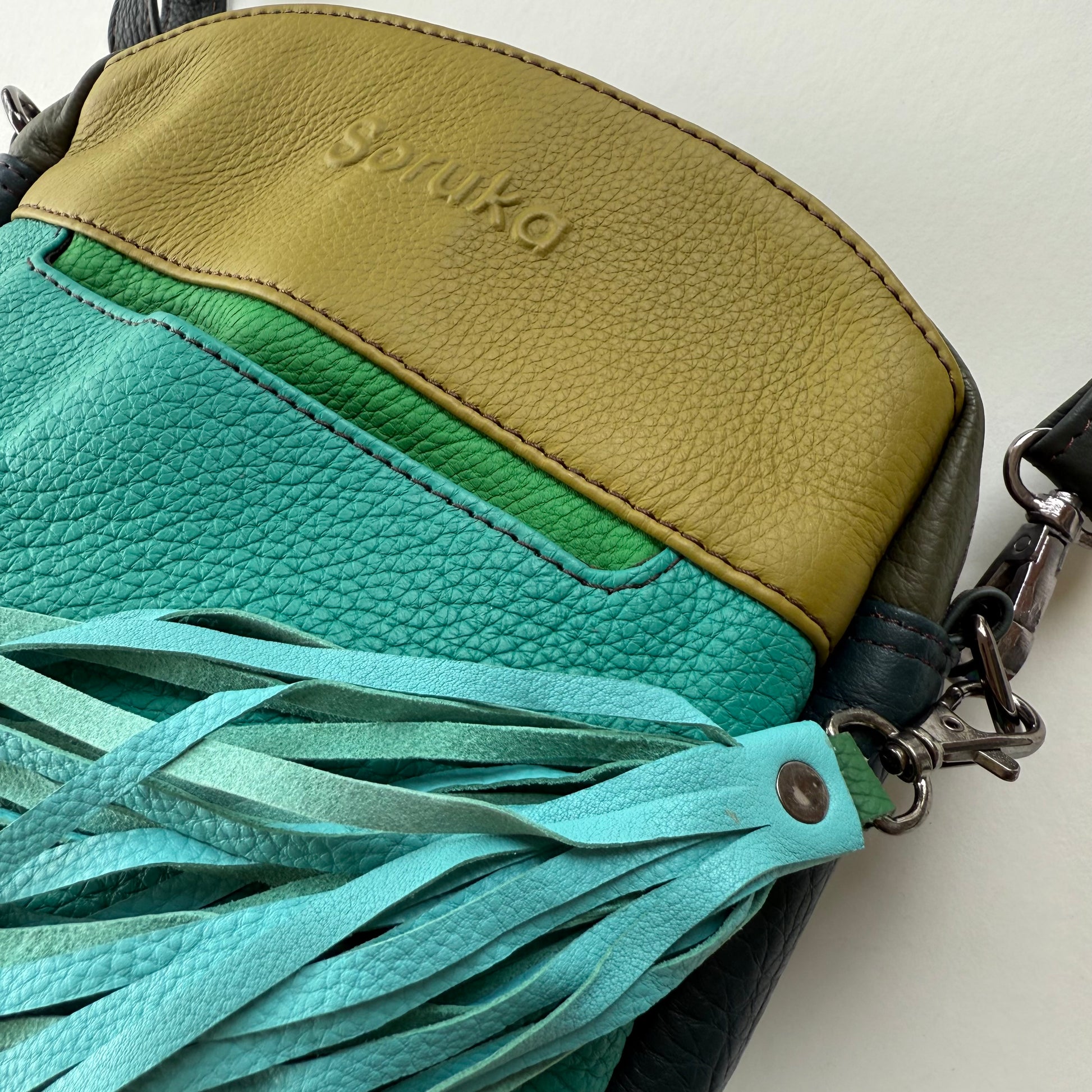 close-up of top of turquoise and lime green handbag with tassel