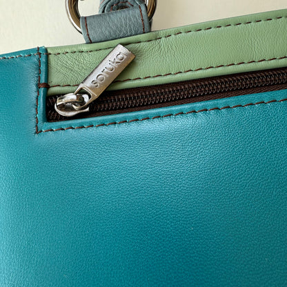 Close-up of a teal and green handbag with zippered pocket