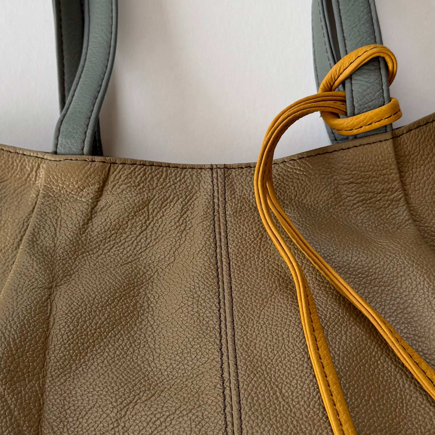 Close-up of a brown leather bag with a yellow tassel strap on a white background