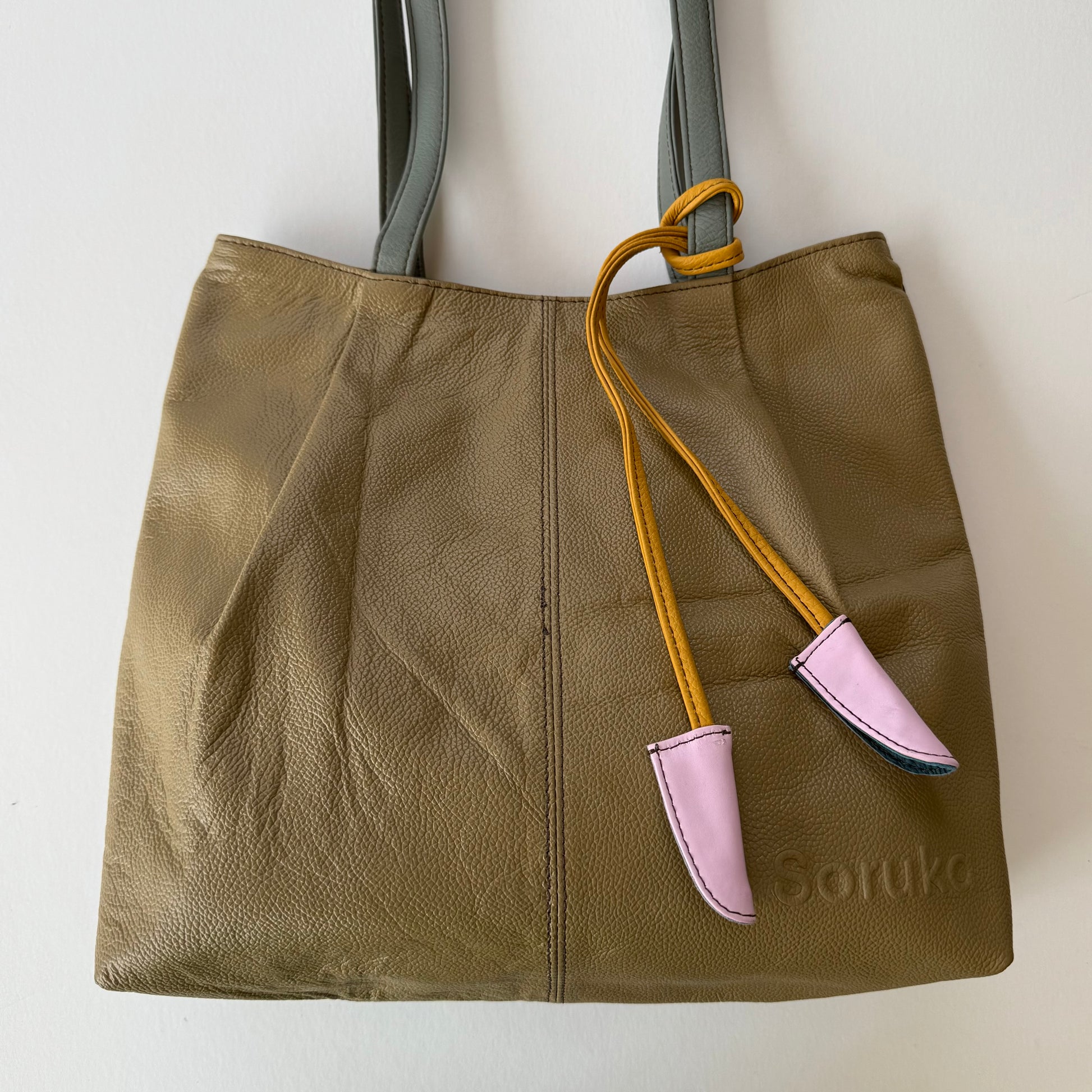 sandy beige tote bag with a yellow and pink accent tassel on a white background