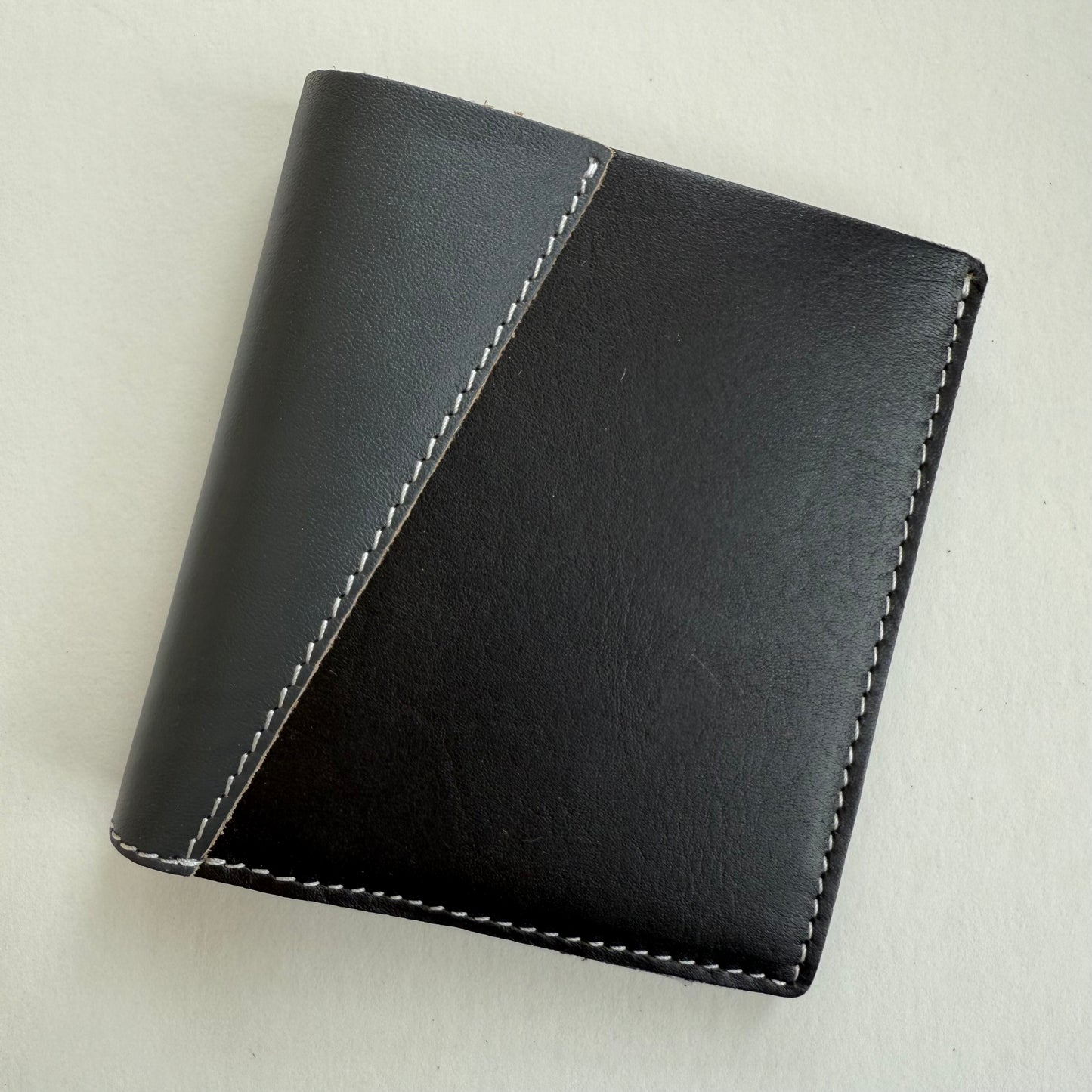 Black and grey leather wallet with white stitching on a light gray background