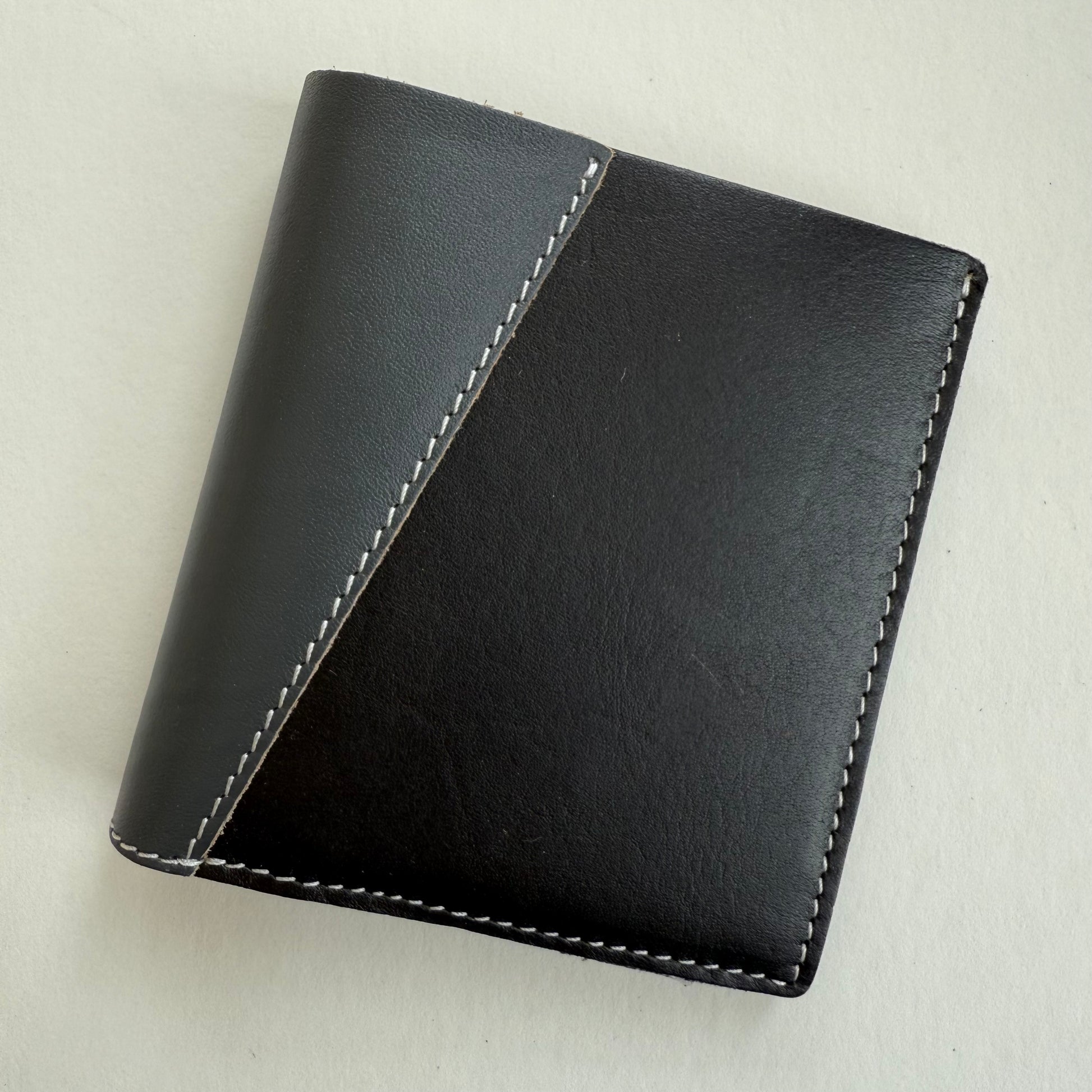 Black and grey leather wallet with white stitching on a light gray background