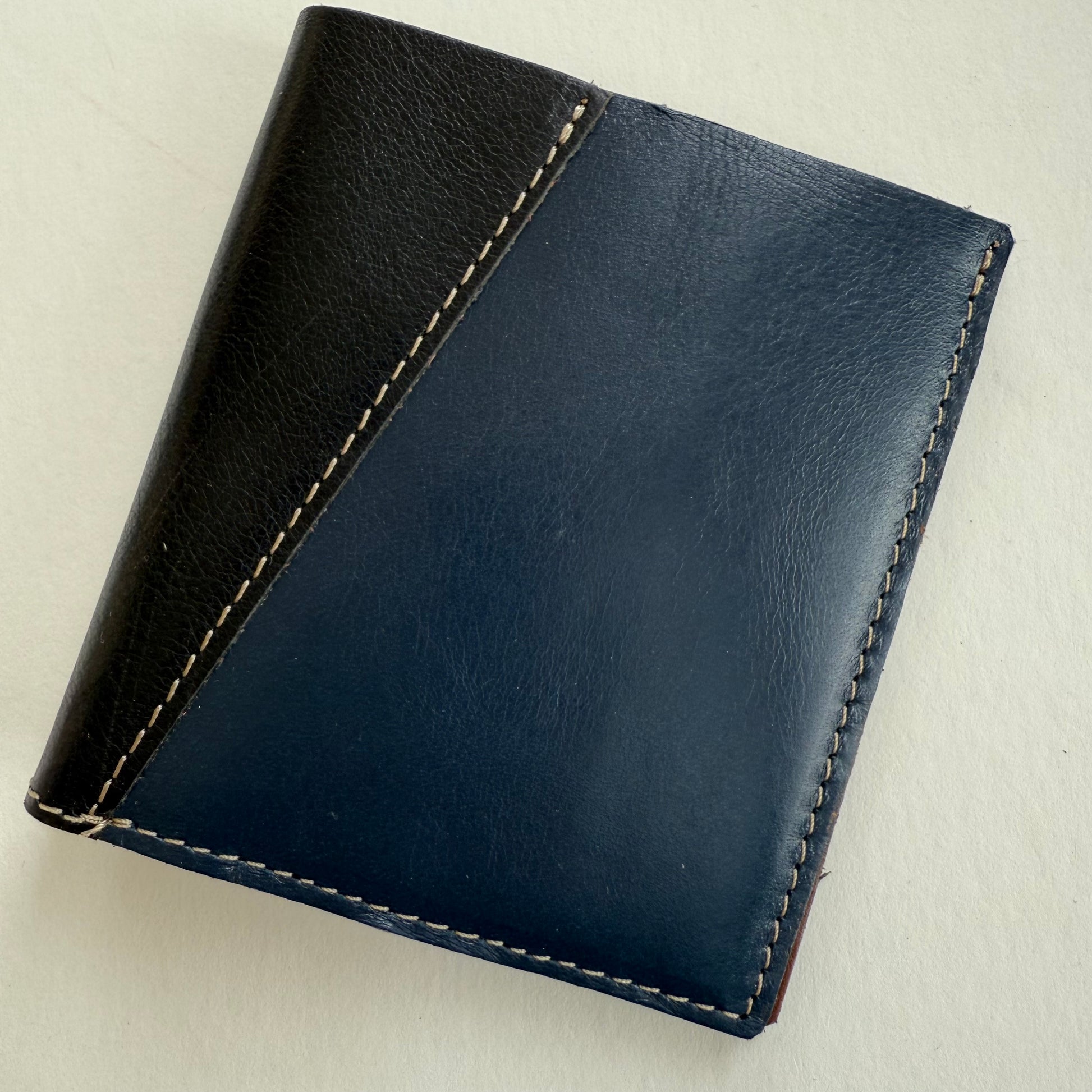 Two-tone black and blue leather wallet on a light beige background