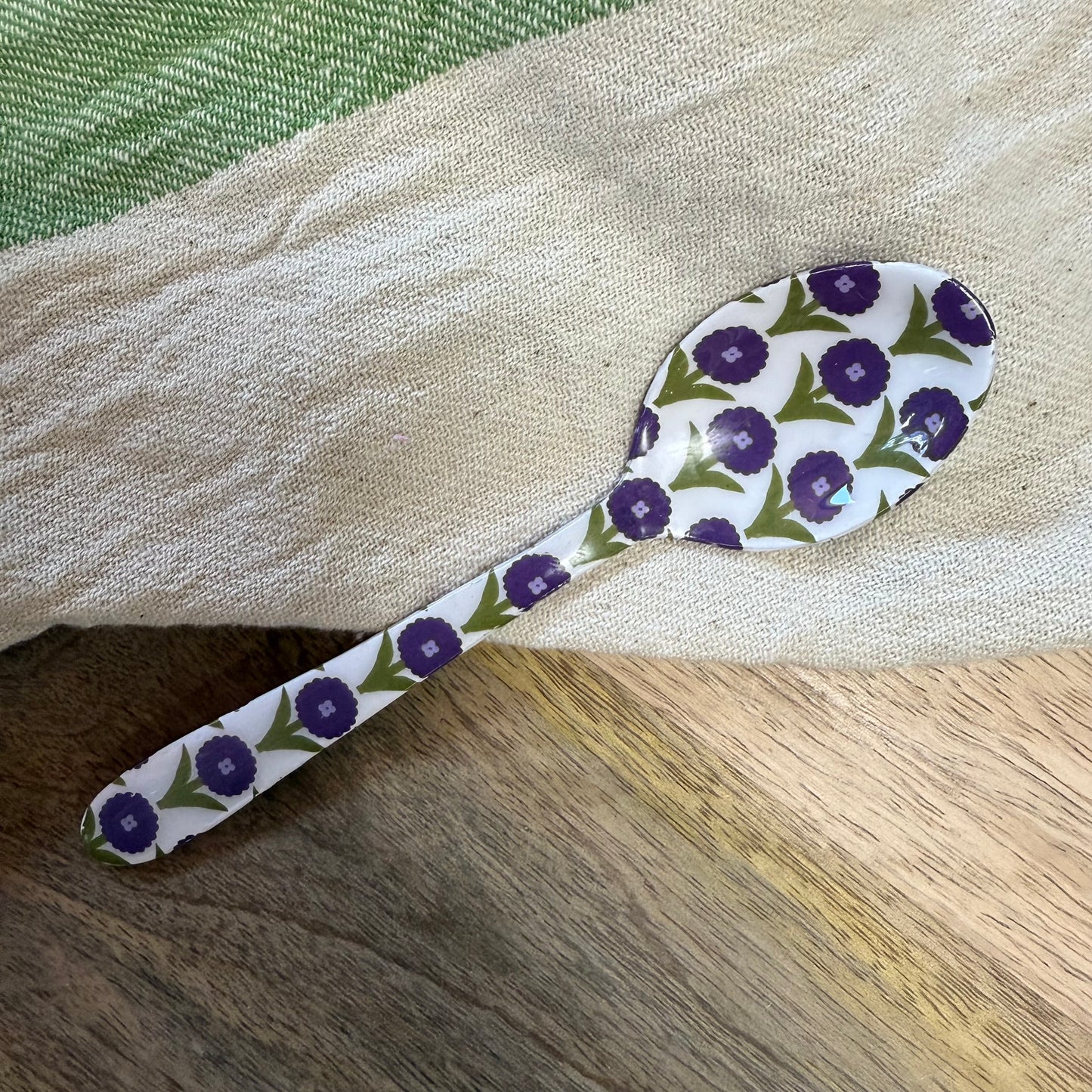 small spoon with purple and green floral pattern on a wood surface with a kitchen towel.