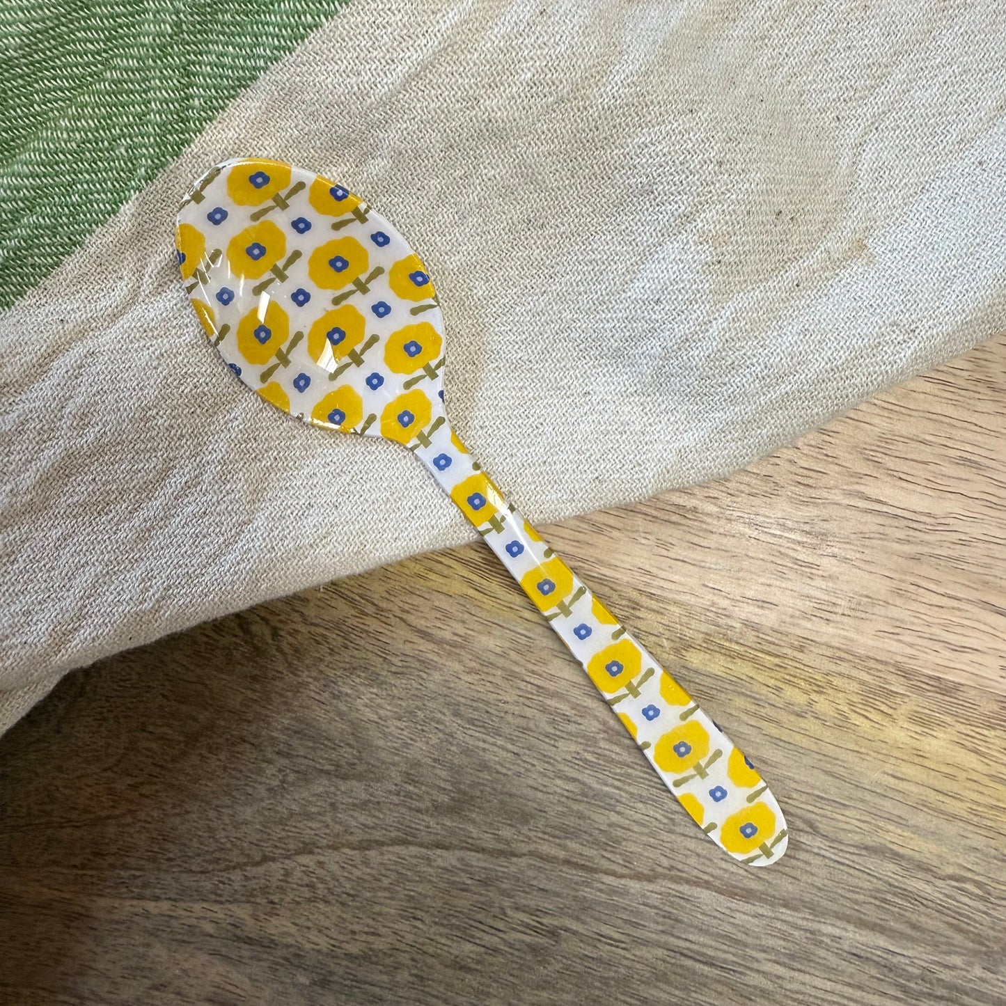 small spoon with yellow and blue floral pattern on a wood surface with a kitchen towel.