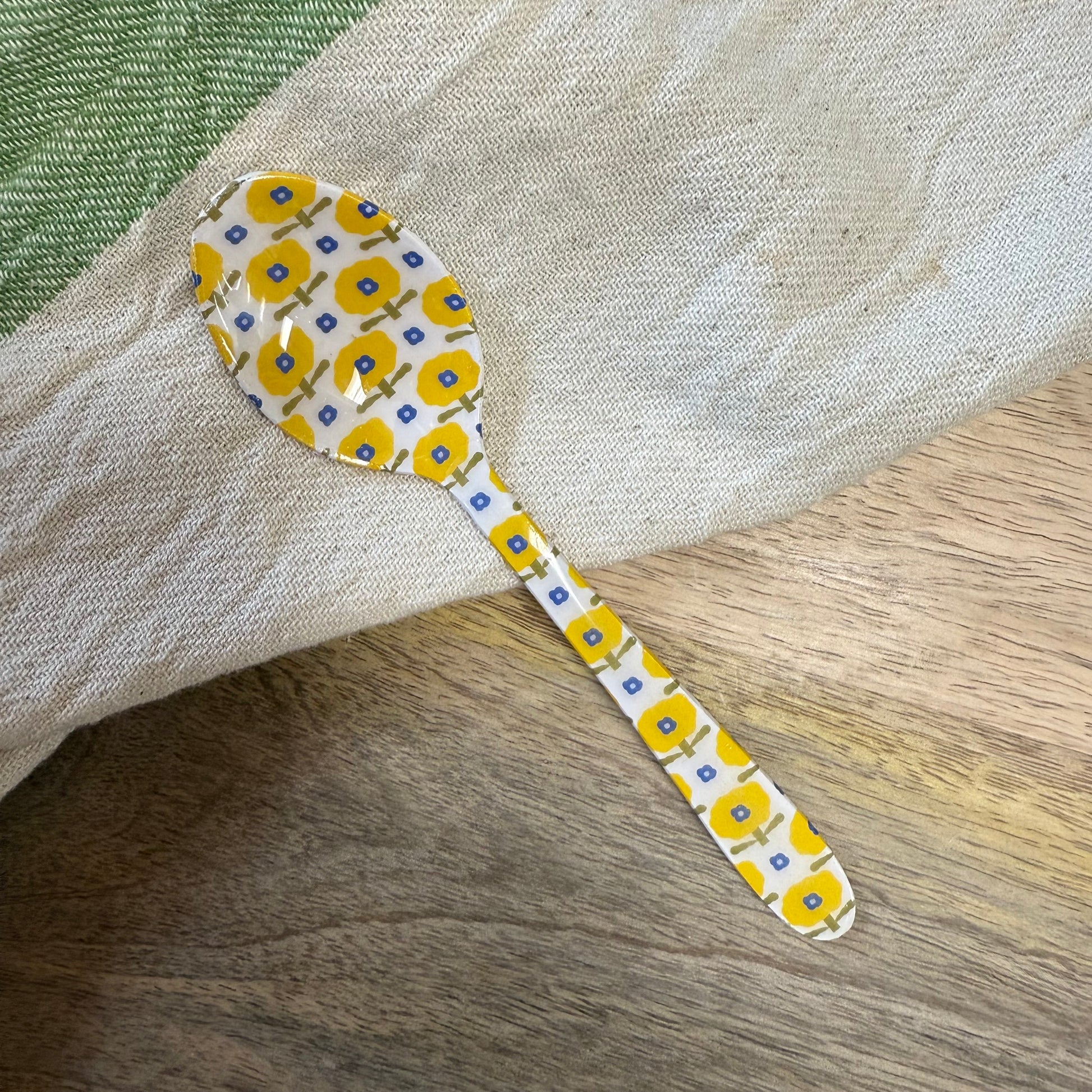 small spoon with yellow and blue floral pattern on a wood surface with a kitchen towel.