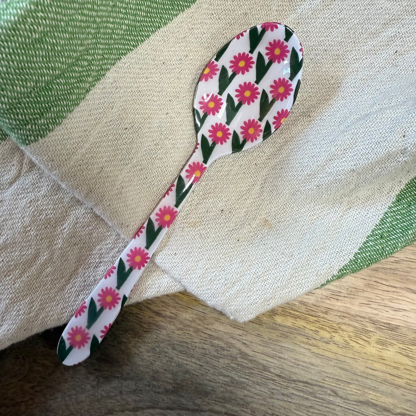 small spoon with pink floral pattern on a wood surface with a kitchen towel.