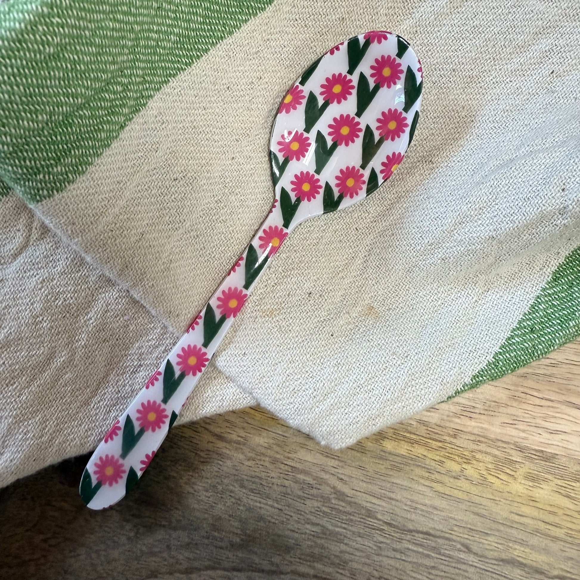 small spoon with pink floral pattern on a wood surface with a kitchen towel.
