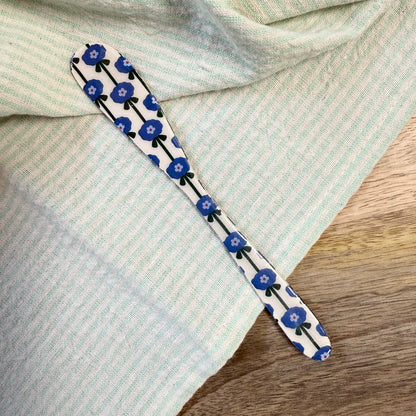 white spreader with blue floral pattern laying on a wooden surface with green striped towel