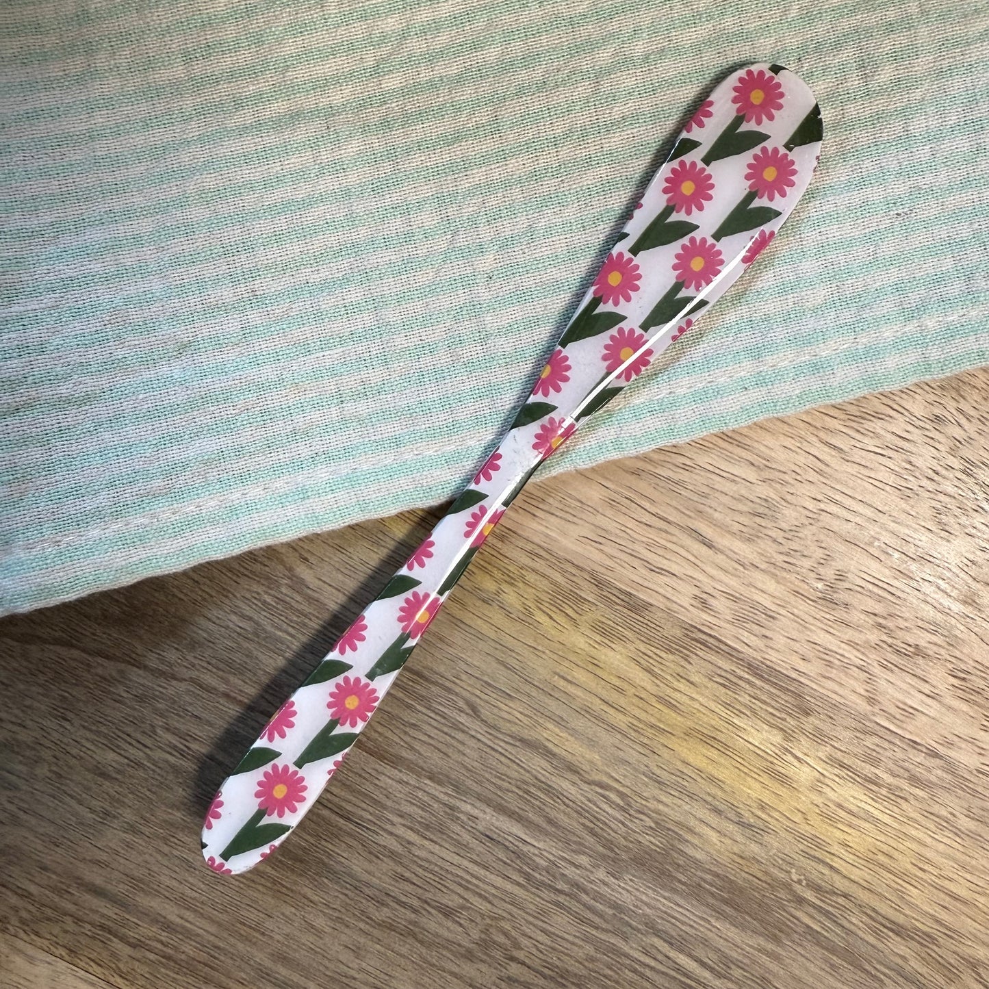 white spreader with pink and green floral pattern laying on a wooden surface with green striped towel