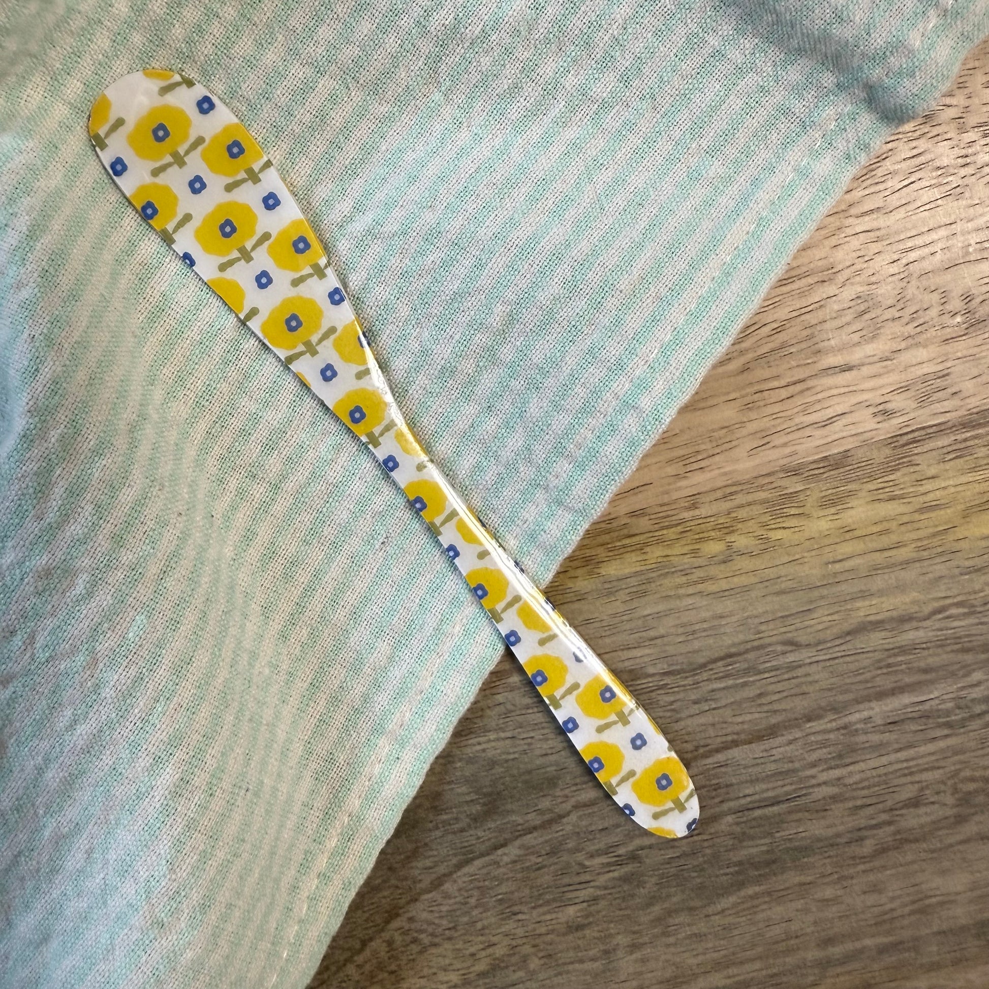 white spreader with yellow floral pattern laying on a wooden surface with green striped towel