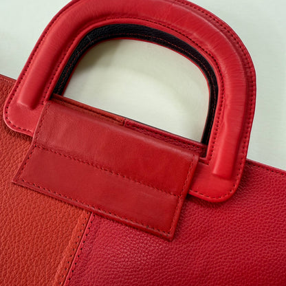 Close-up of a red tote bag handle and leather texture.