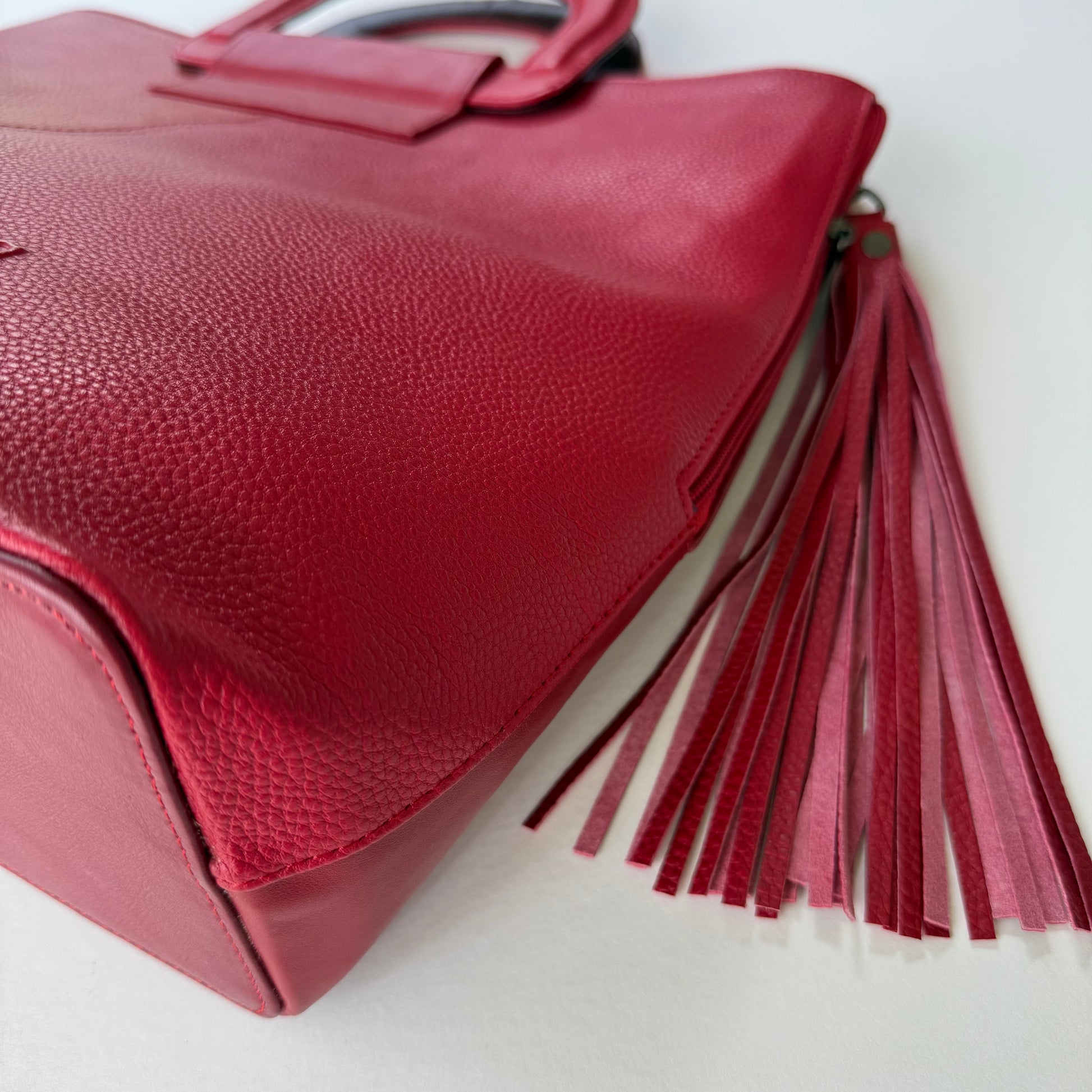 close-up of bottom corner of Red tote bag with a tassel on a white background