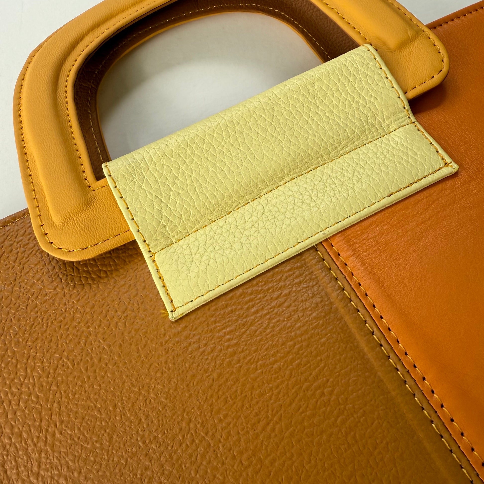 Close-up of yellowish-brown leather bag with a yellow handle.