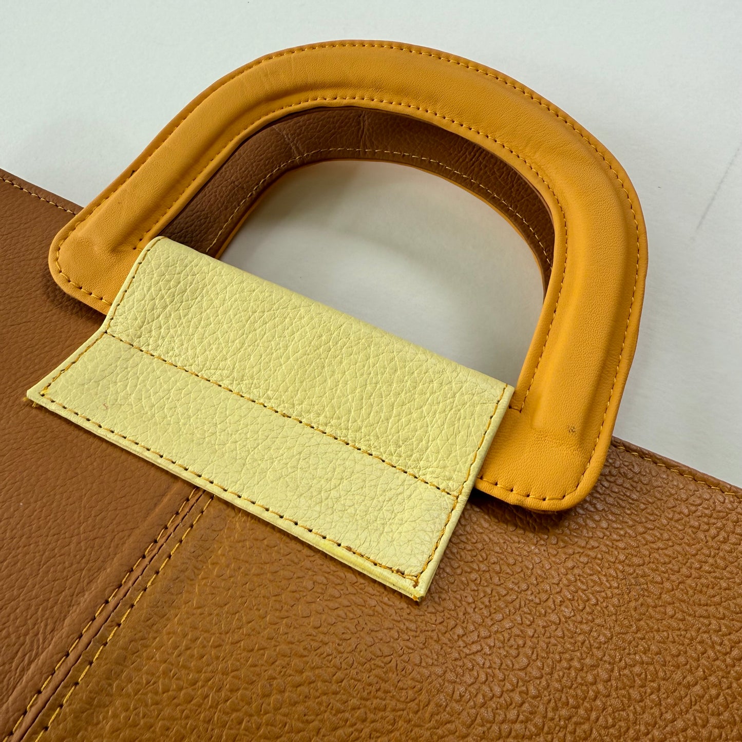 Close-up of a yellow-brown leather bag with a yellow handles