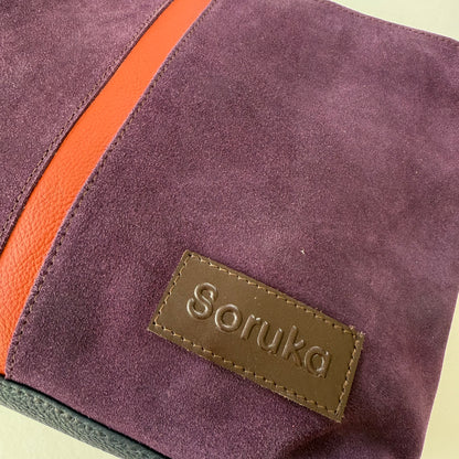 Close-up of a purple suede bag with a dark orange zipper and 'Soruka' brand label.