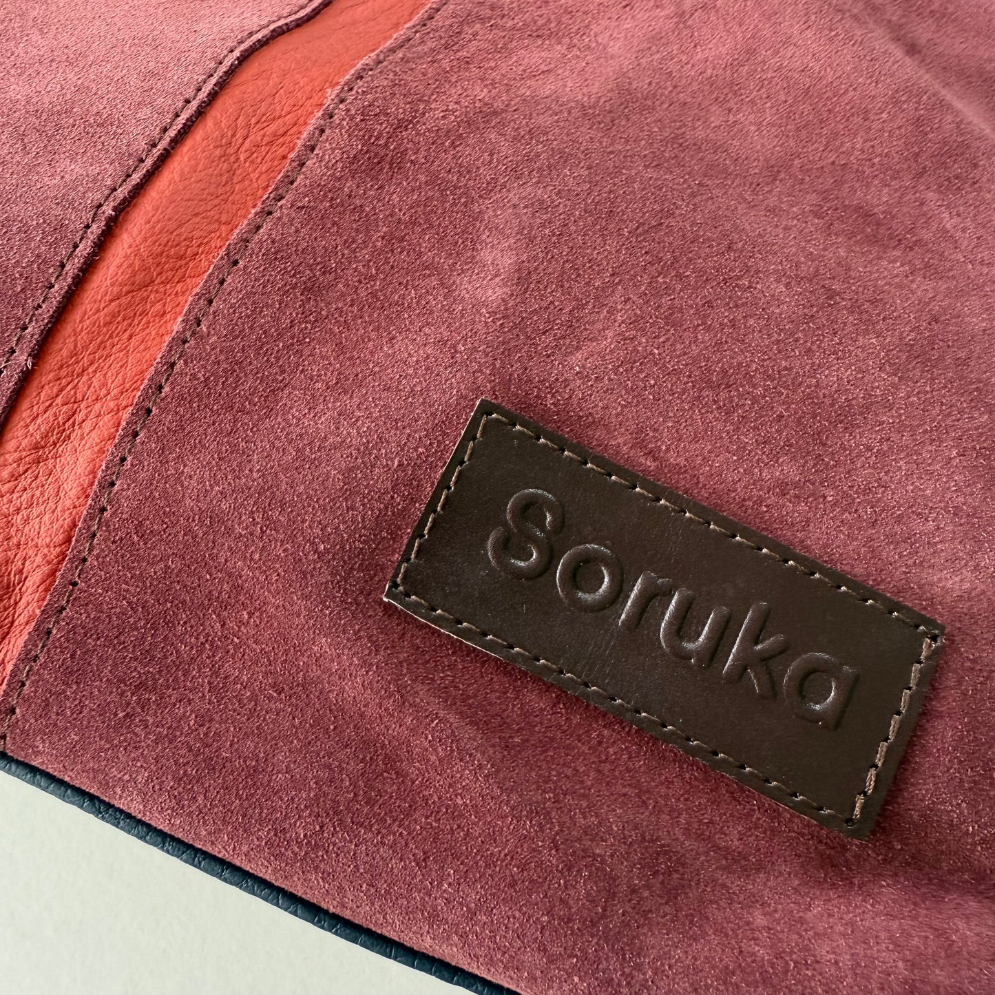 Close-up of a maroon suede bag with 'Soruka' branding.