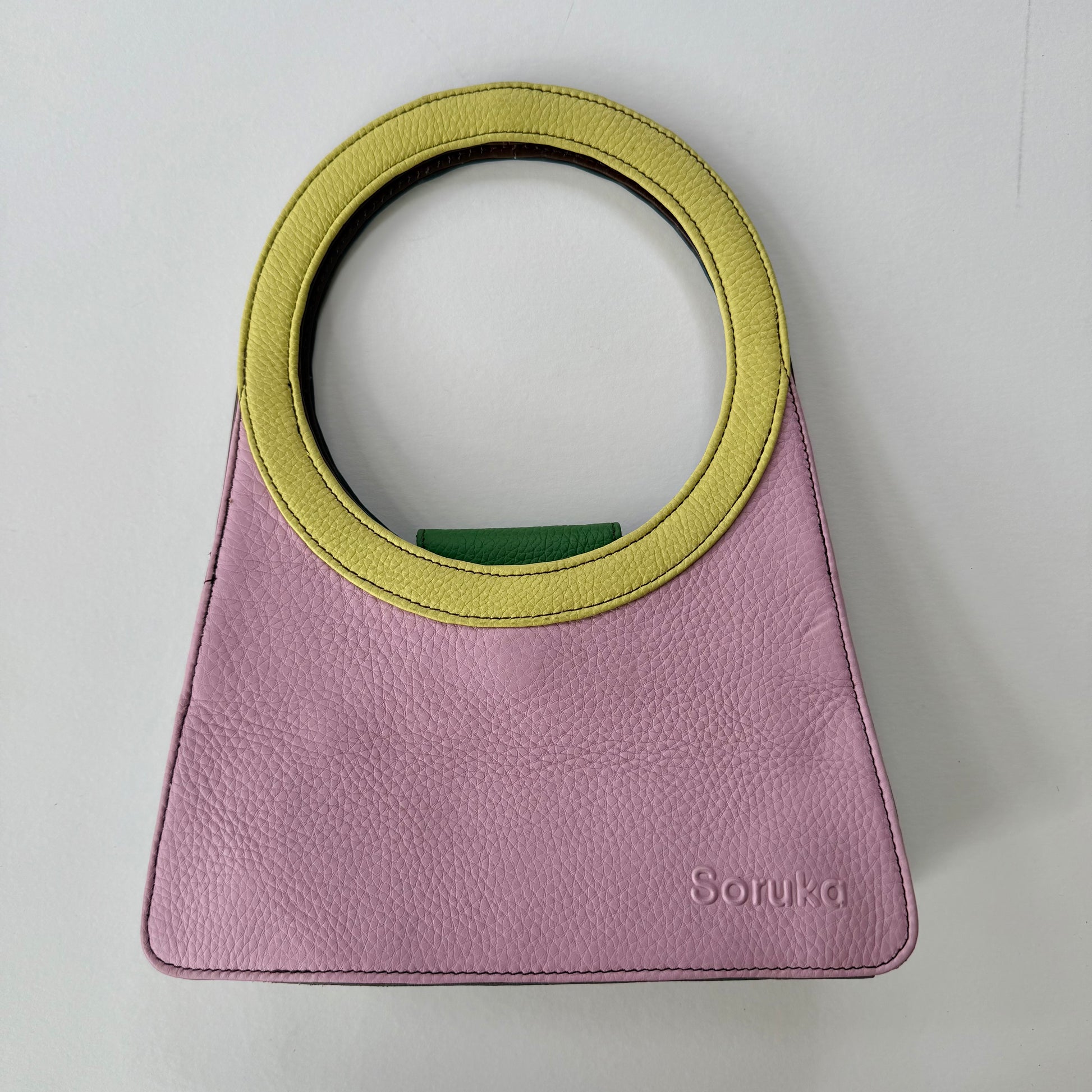 Pink handbag with a yellow circular handle on a light gray background