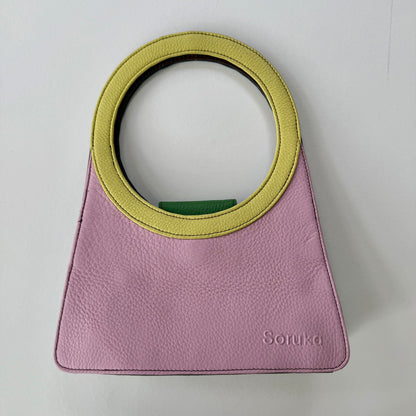Pink handbag with a yellow circular handle on a light gray background