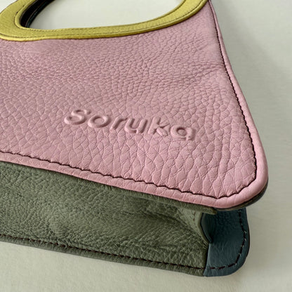 Close-up of a pink and green leather handbag with 'Sorukka' branding on a light background
