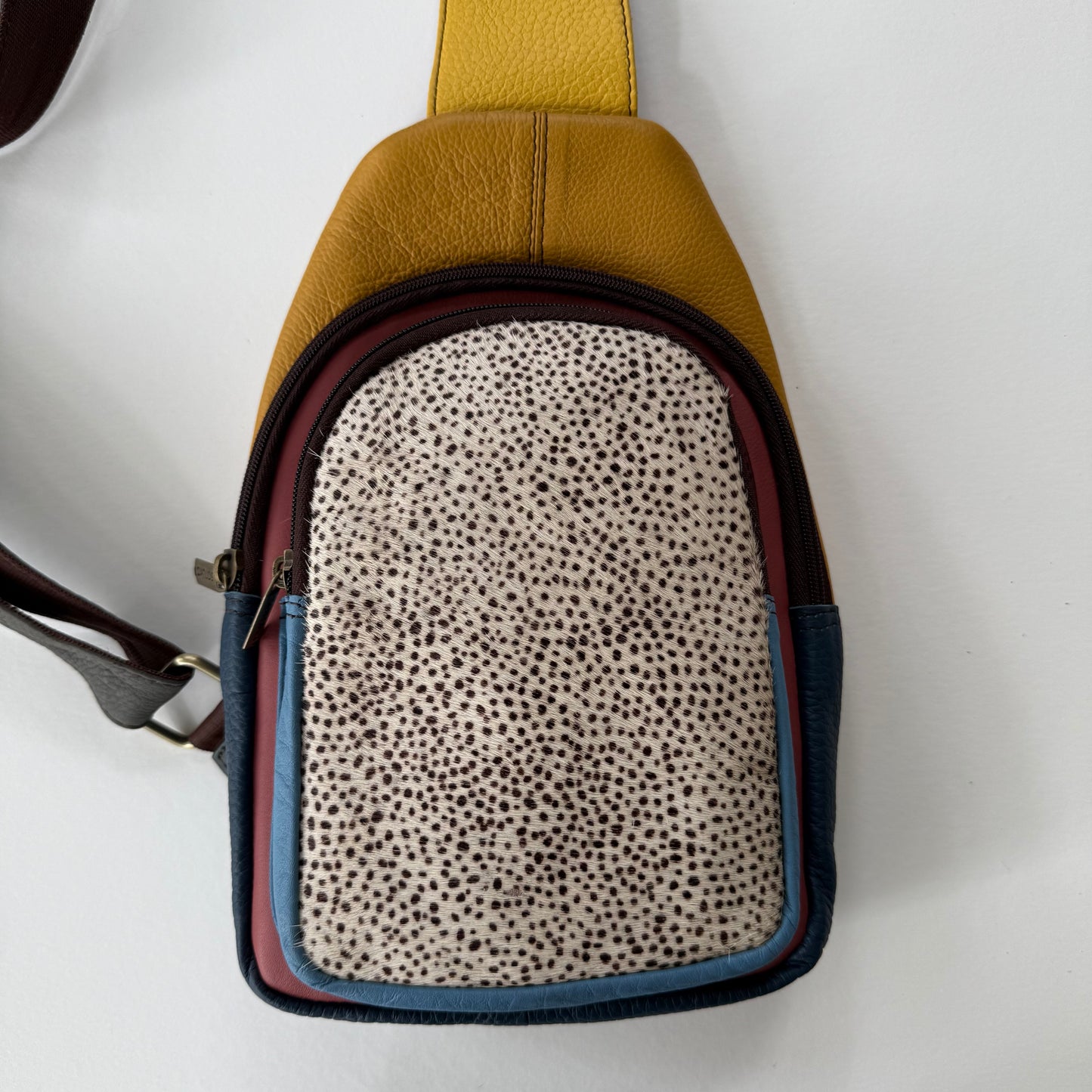 Sling bag in a patch work of colors with spotted pattern front pocket