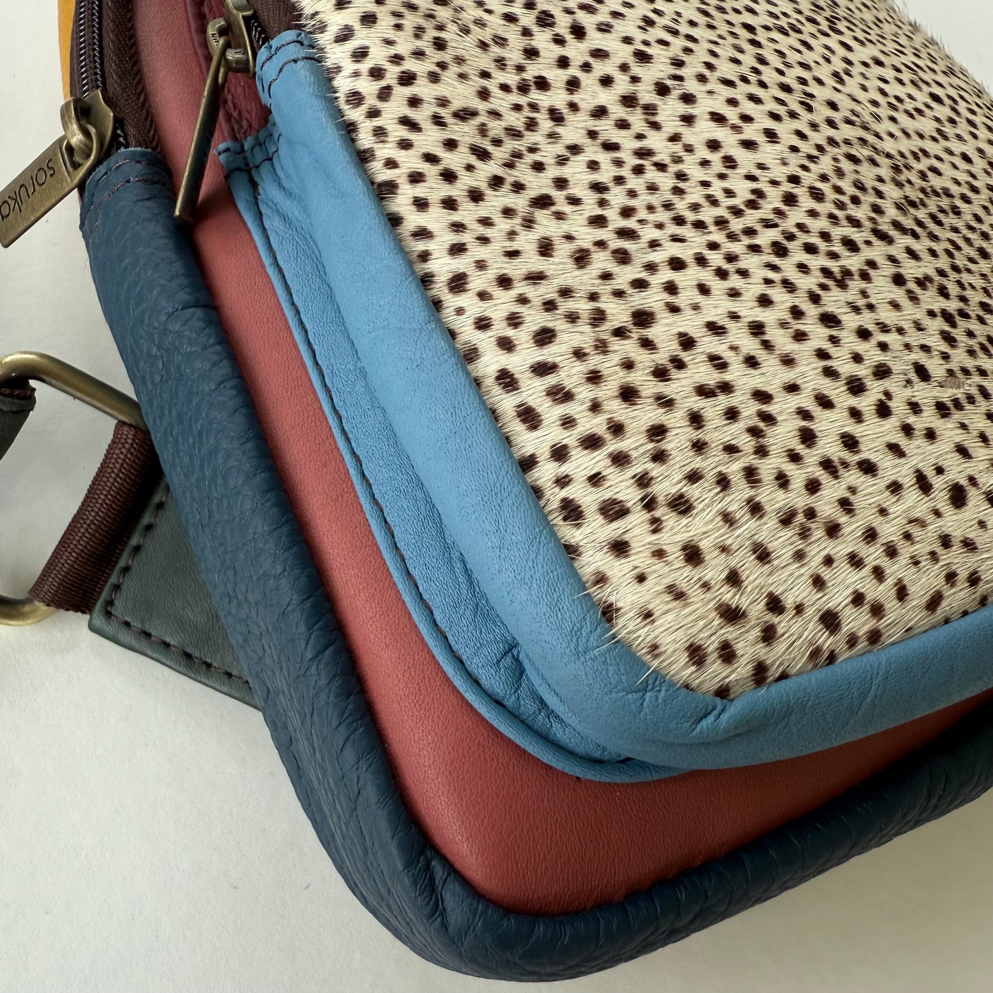 close-up of bottom corner of sling bag in multiple colors