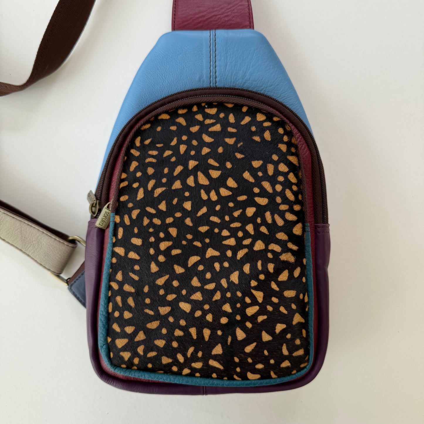 blue and purple sling bag with black and brown animal pattern front pocket