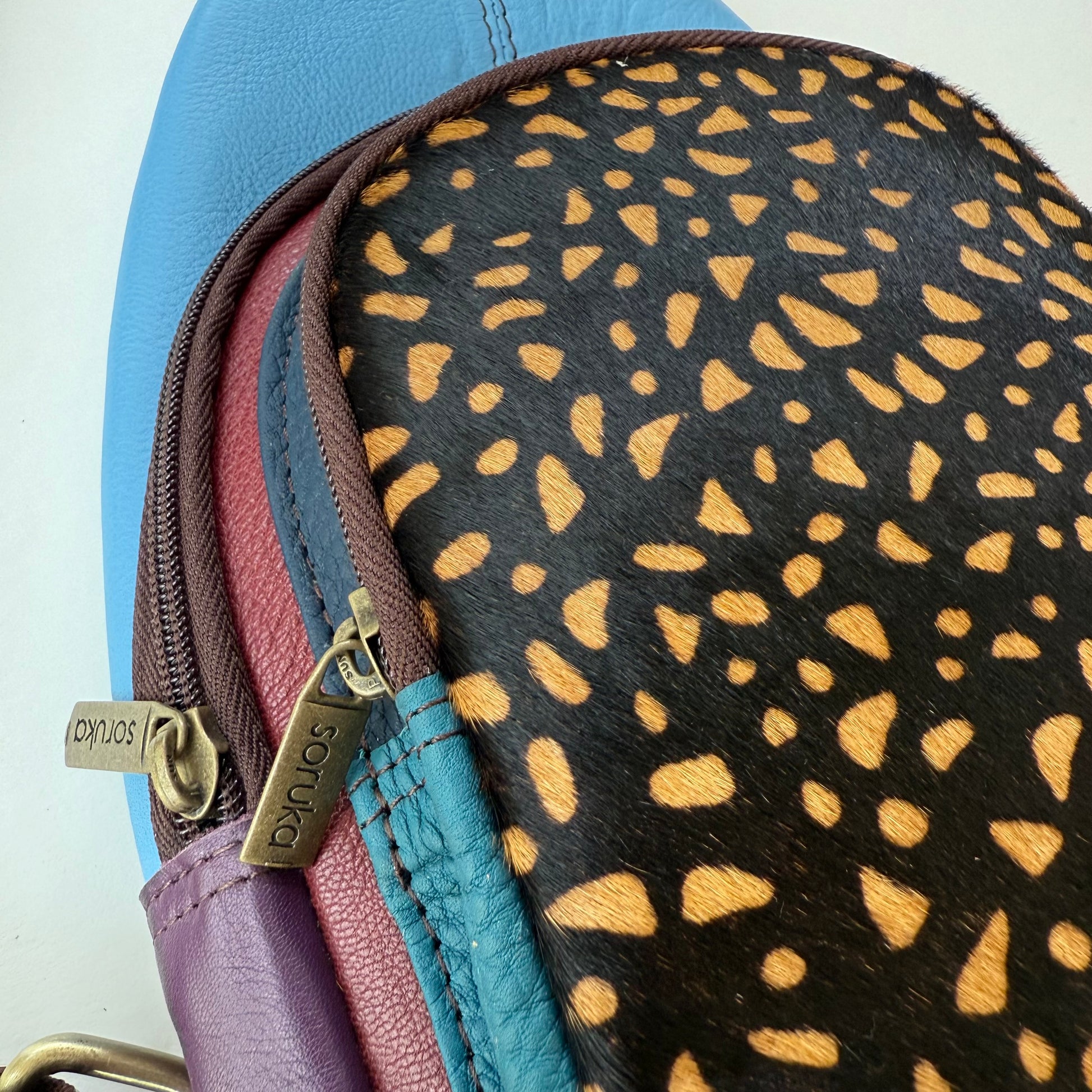close-up of multi-colored sling bag showing 2 zippered compartments