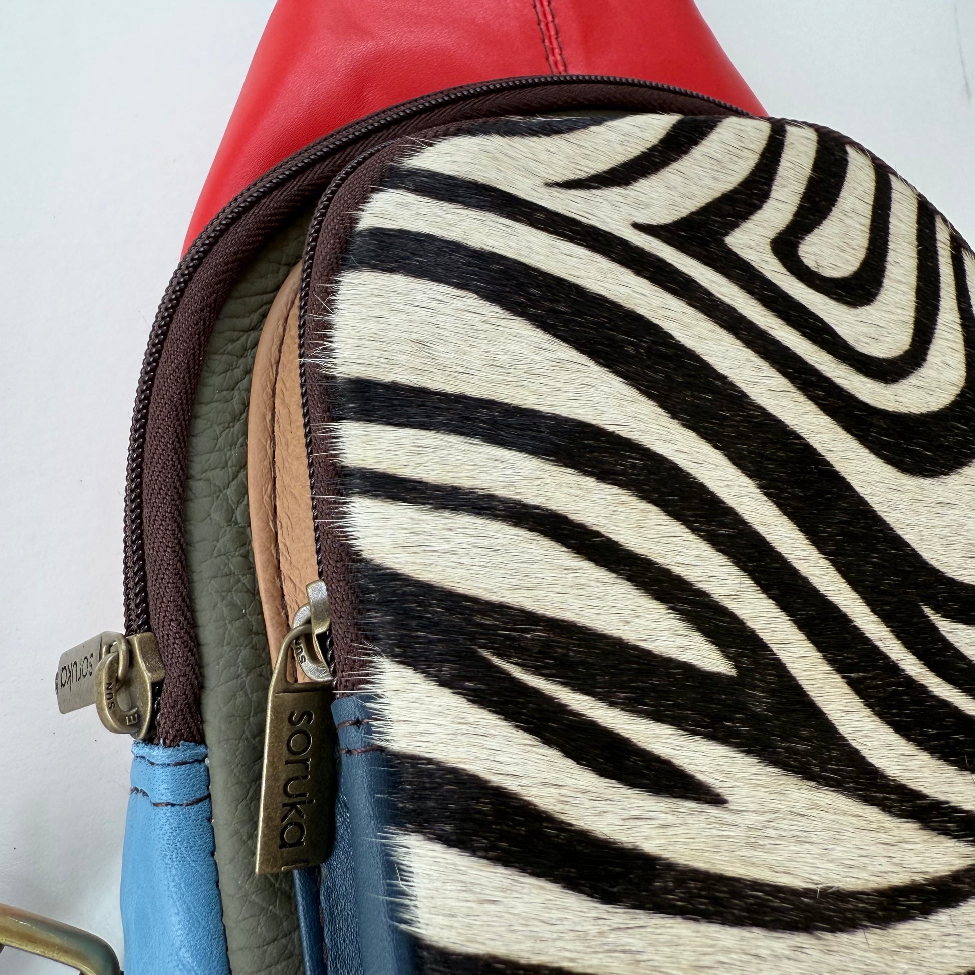 Close-up of side view of red and blue sling bag with zebra-patterned showing 2 zipper compartments