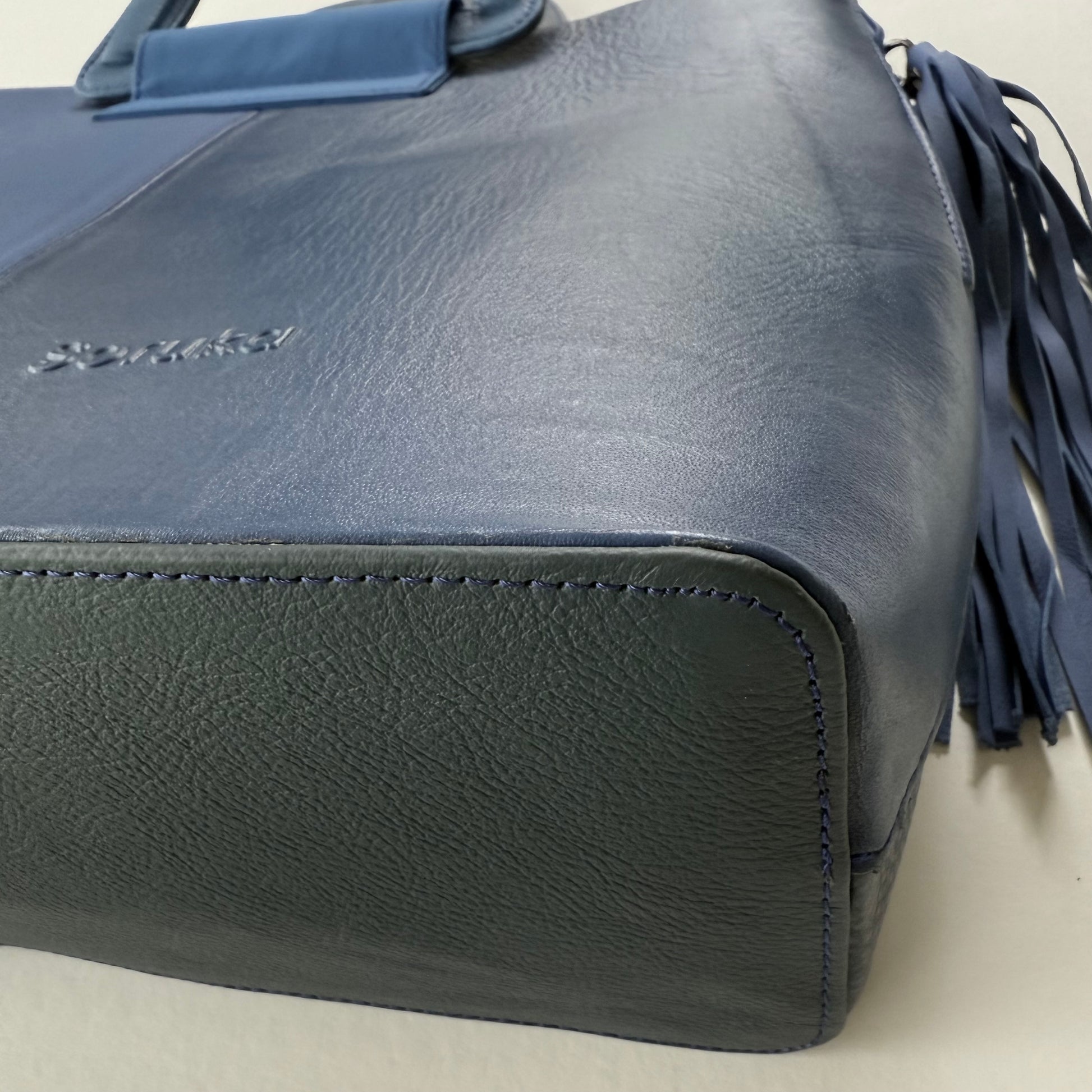close-up of bottom corner of Blue leather tote bag with tassel