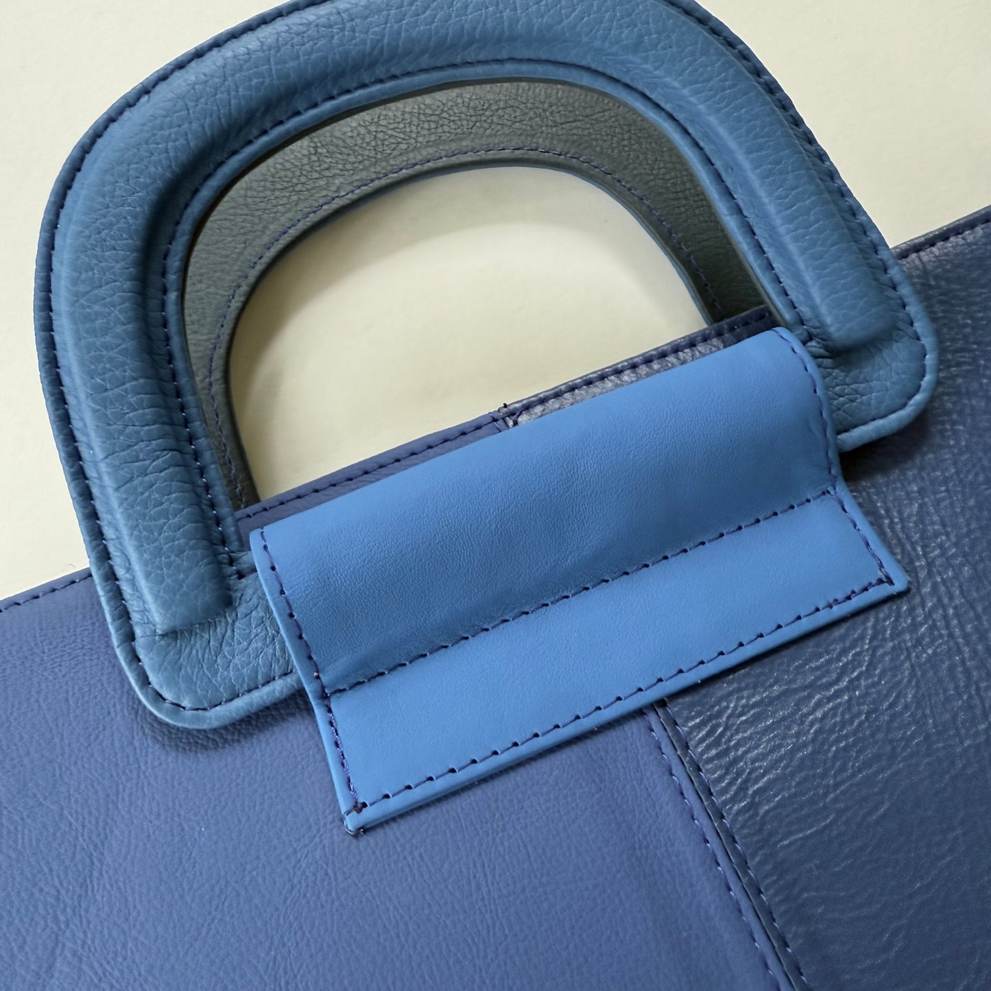 Close-up of a blue leather tote bag handle on a beige background