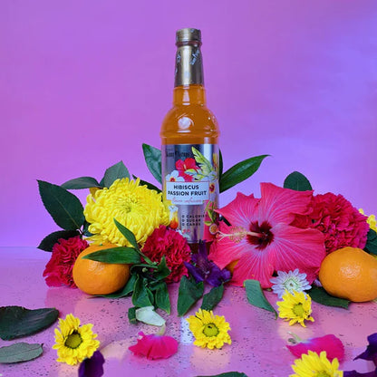 bottle of Hibiscus Passion Fruit skinny syrup arranged with fruit and flowers.