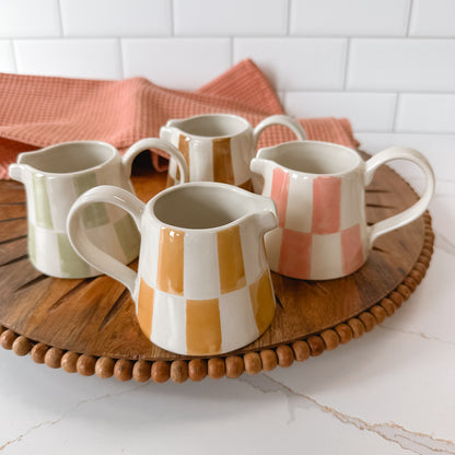 ceramic cream pitchers with checked pattern set on a wooden board with a dishtowel in the background