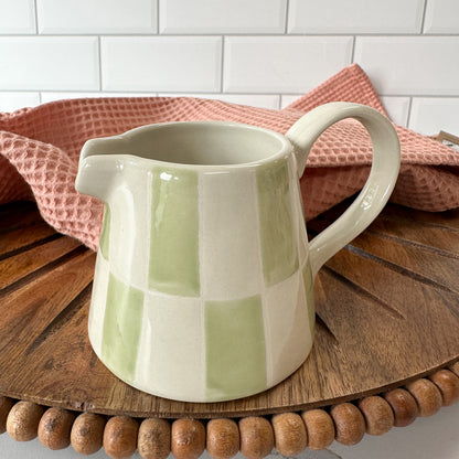 ceramic creamer with green and cream checked pattern set on a wooden board