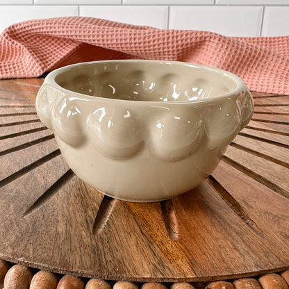 taupe ceramic little bowl with a raised dotted rim set on a wooden board