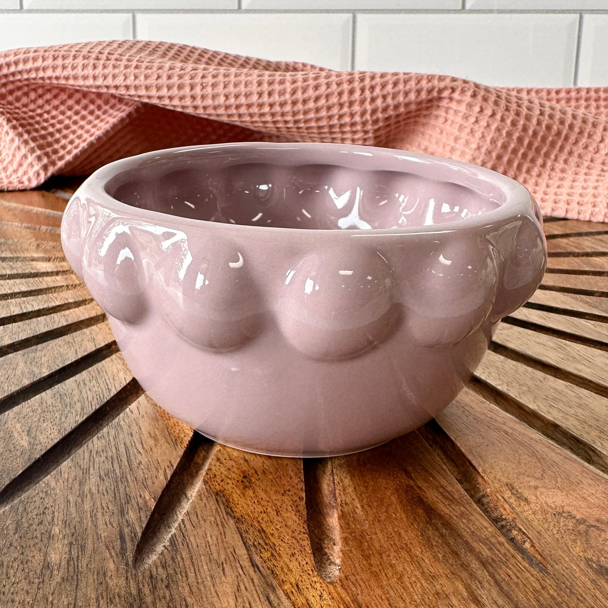 lavender ceramic little bowl with a raised dotted rim set on a wooden board