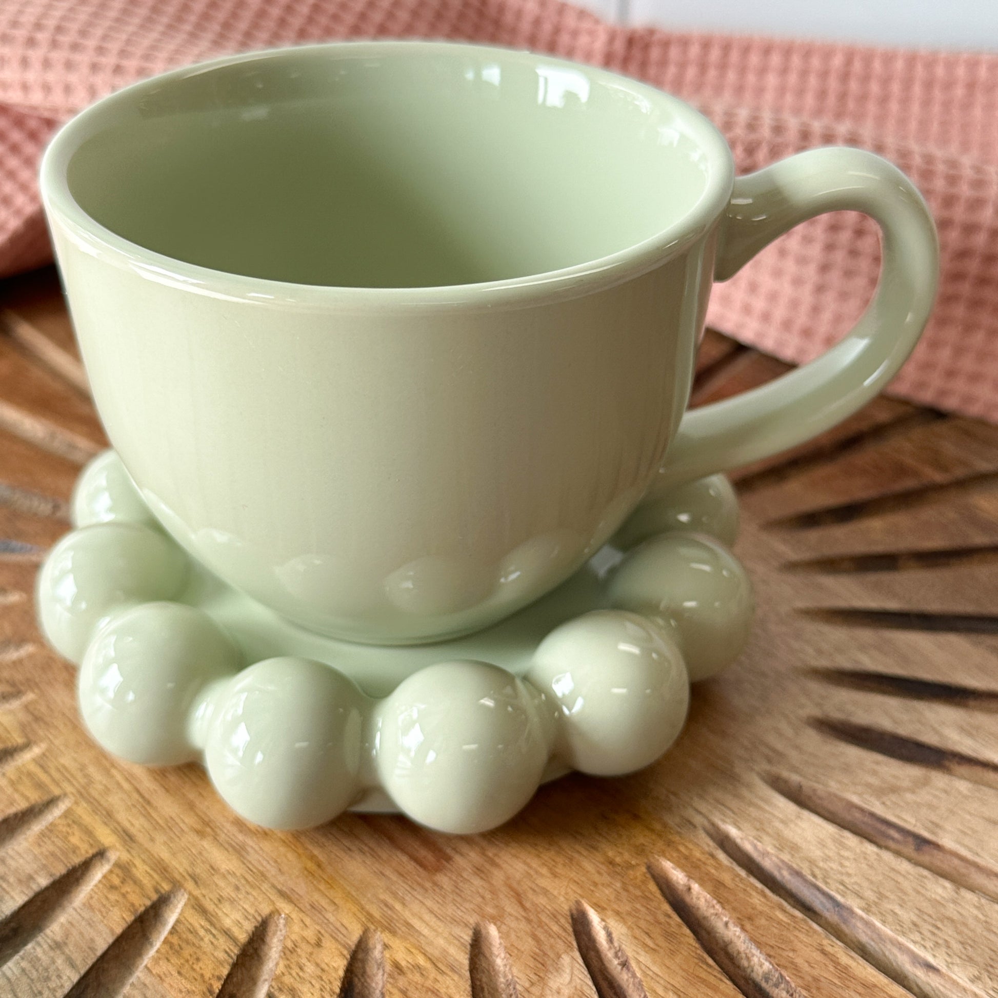 sage green Stoneware Mug with Bubble Saucer set on a wooden board