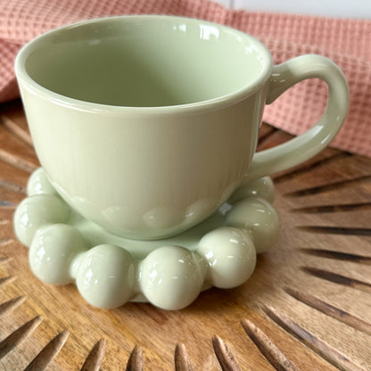 sage green Stoneware Mug with Bubble Saucer set on a wooden board