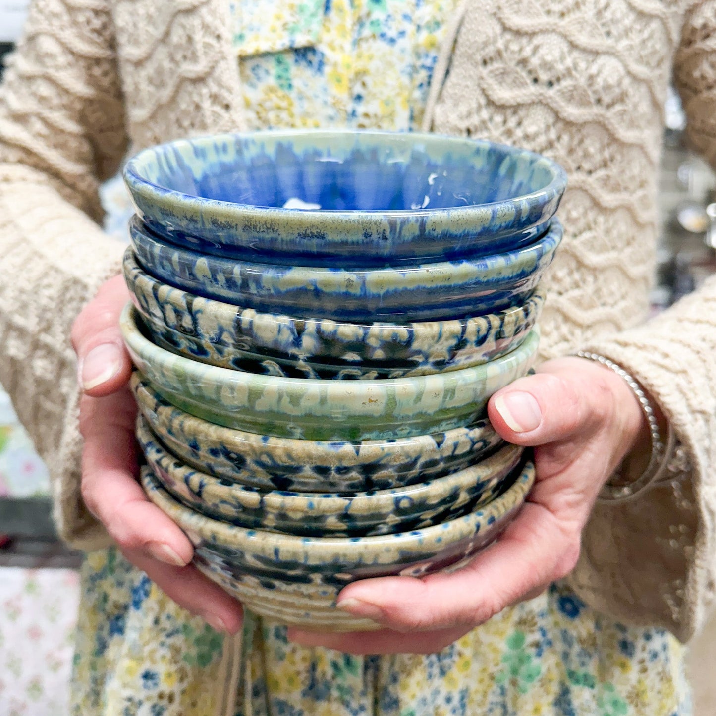 Stack of ceramic bowls held by a person wearing a patterned garment.