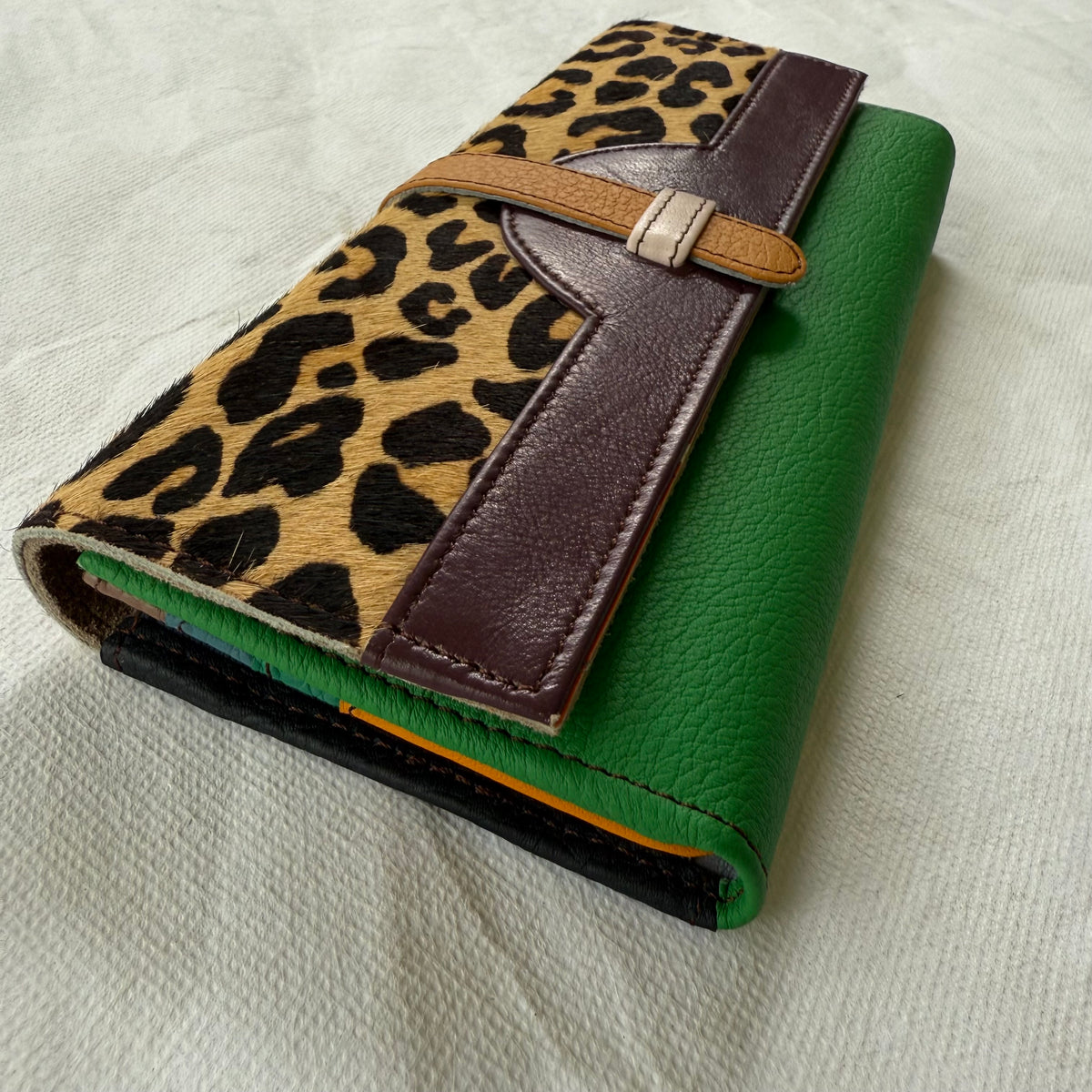 side view of leather wallet with a green body, a leopard-print flap, and dark maroon leather trim