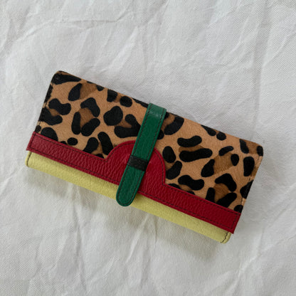A multicolor leather wallet featuring a leopard print pattern on the top flap, a red leather band, a yellow leather base
