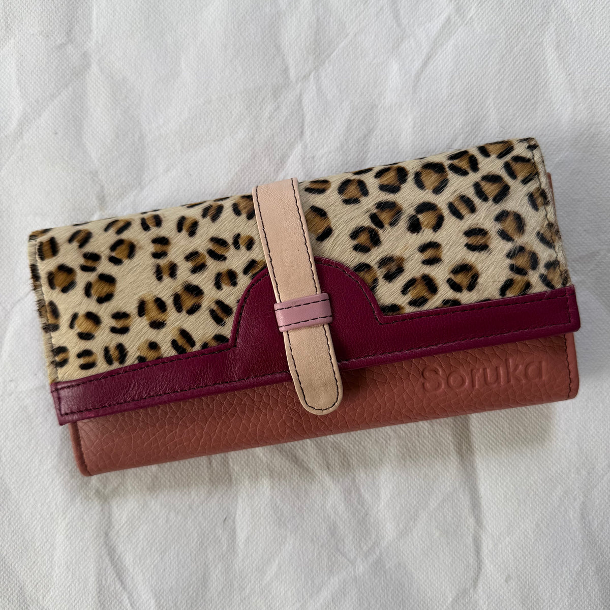 A long wallet with a leopard print top section, a burgundy leather band, and mauve body