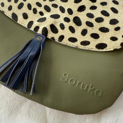 Close-up of a Soruka bag featuring an olive green leather body, a beige and black leopard-print flap, and a navy blue leather tassel.