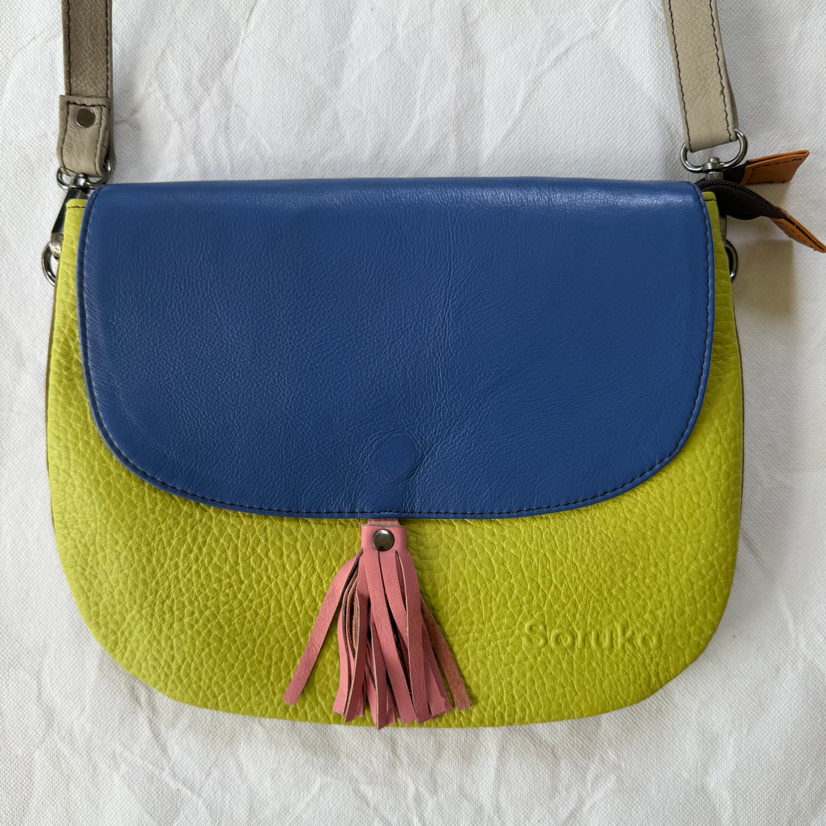A pebbled leather shoulder bag with a bright lime green body, a blue flap, and a pink tassel 
