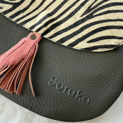 Close-up of a Soruka bag featuring a grey pebbled leather body, a pink leather tassel, and a beige and black zebra-print flap.