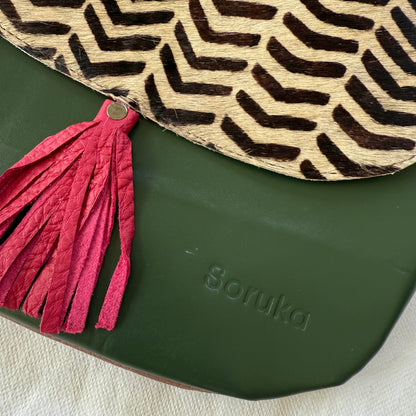 Close-up of a Soruka bag featuring a dark green leather base, a pink leather tassel, and a beige and black chevron-patterned leather flap.
