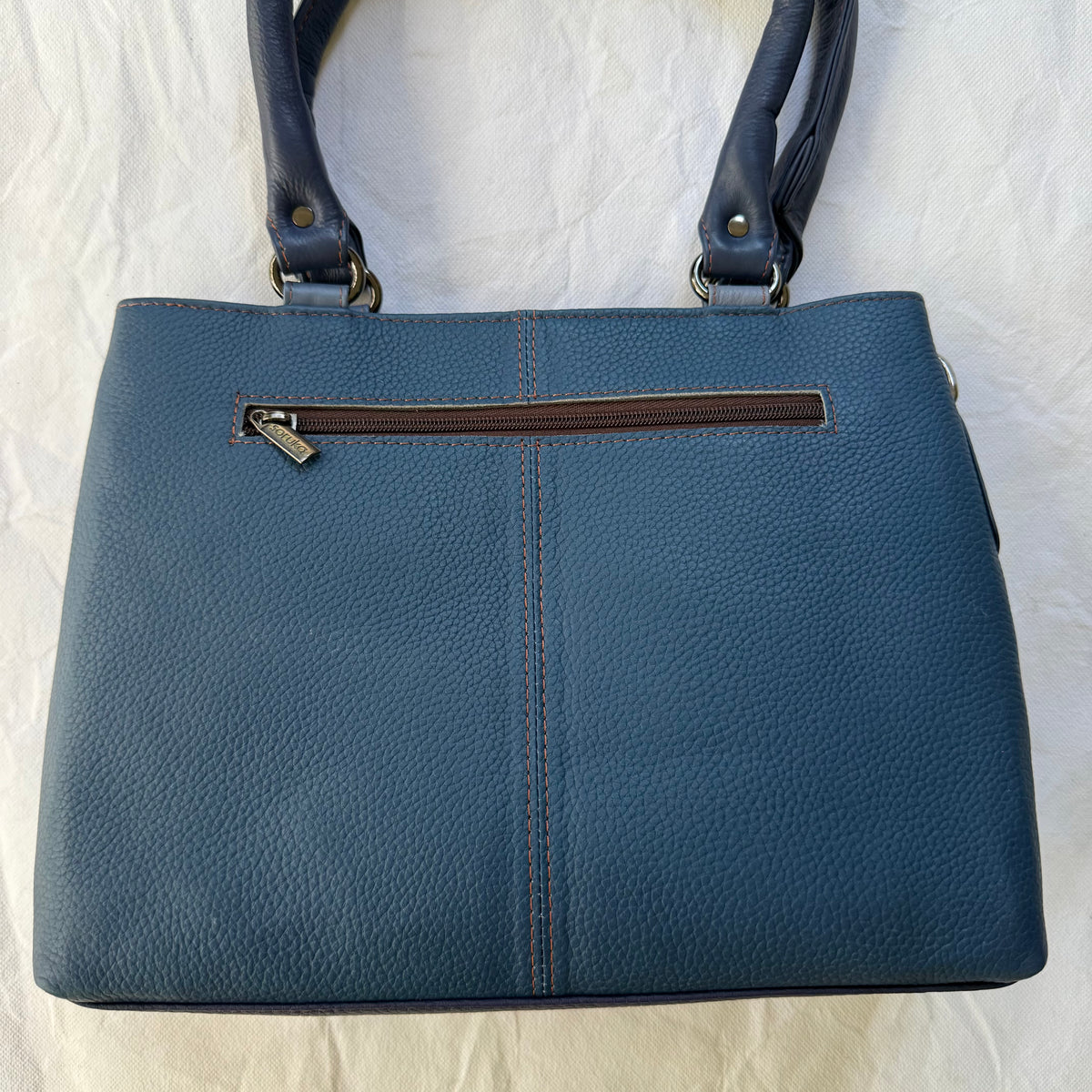 other side of blue handbag in deep blue leather with a zipper pocket across the top