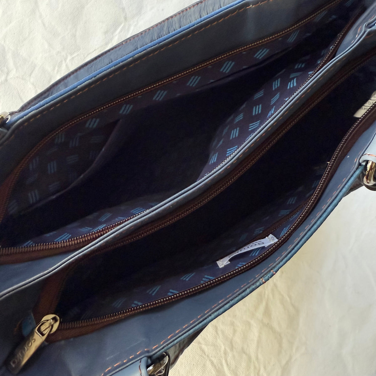 top view of blue handbag with 2 unzipped compartments showing blue patterned interior