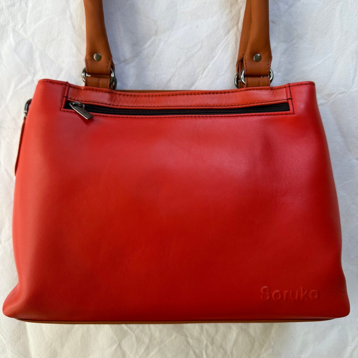 bright orange leather handbag with zip pocket across the top and 2 muted orange shoulder straps
